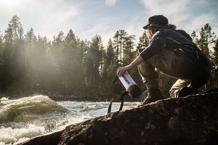 A hiker crouching beside a fast moving river with a LifeSaver Bottle